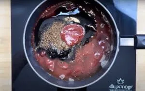 Tomato sauce and spices simmering in a pan on an induction cooktop.